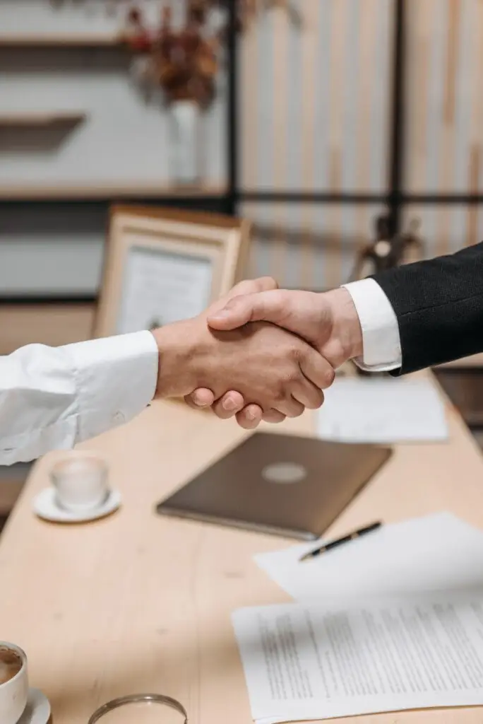 Handshake across a desk next to a signed contract